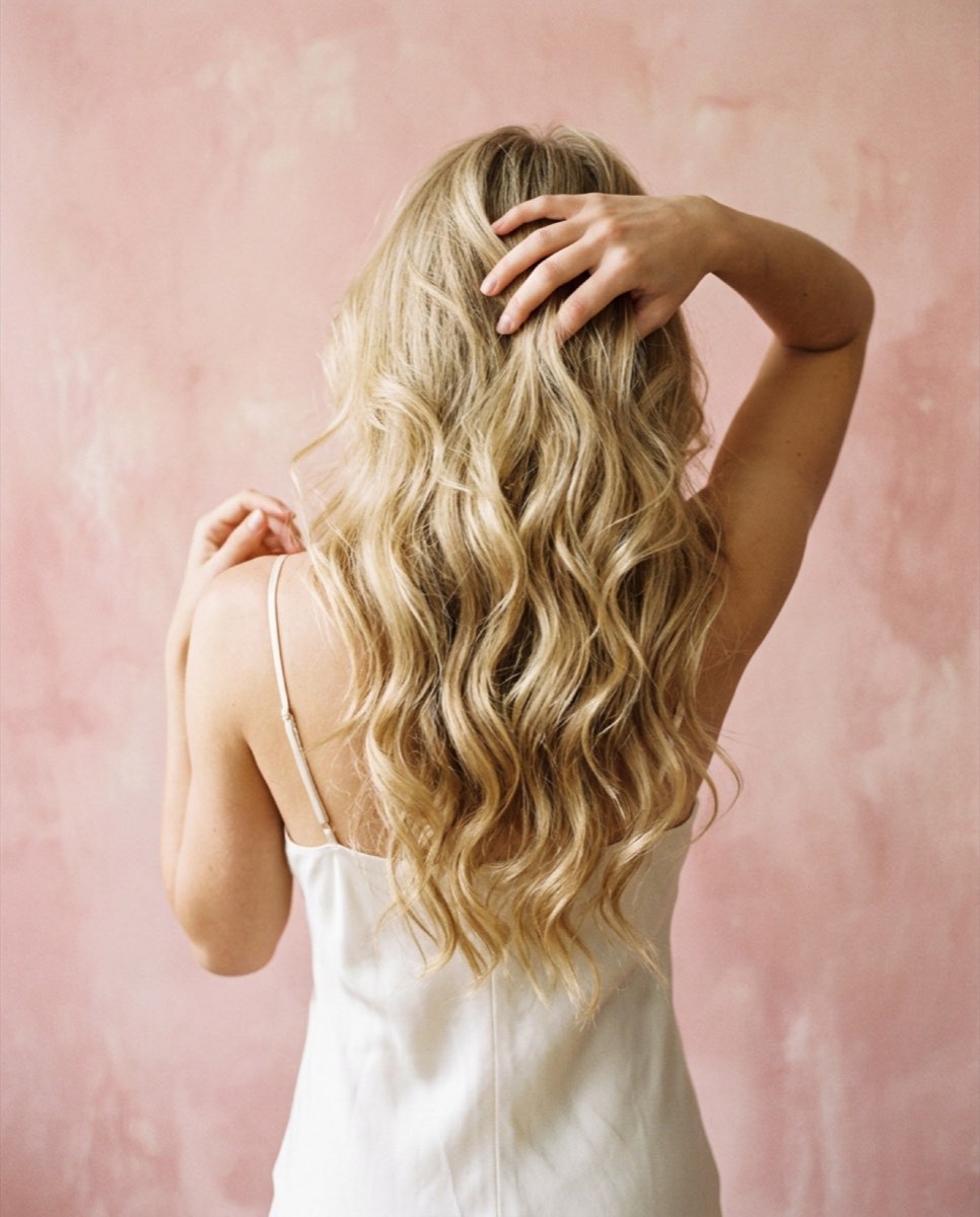 Long blonde waved hair photographed from behind against a pink plaster wall