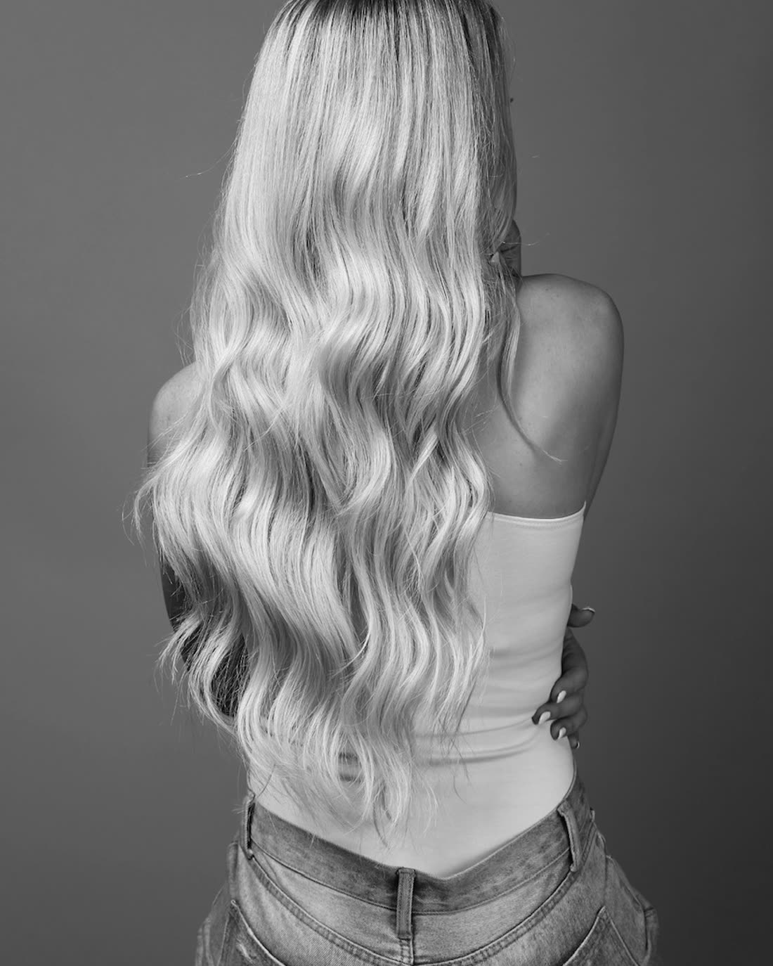 Long blonde tape-in hair extensions waved to the waist, photographed from behind in studio
